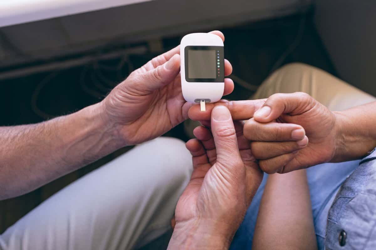 Close-up van een persoon die de hand van een andere persoon vasthoudt terwijl hij een glucometer gebruikt om zijn bloedsuikerspiegel te controleren, met een teststrip in het apparaat.