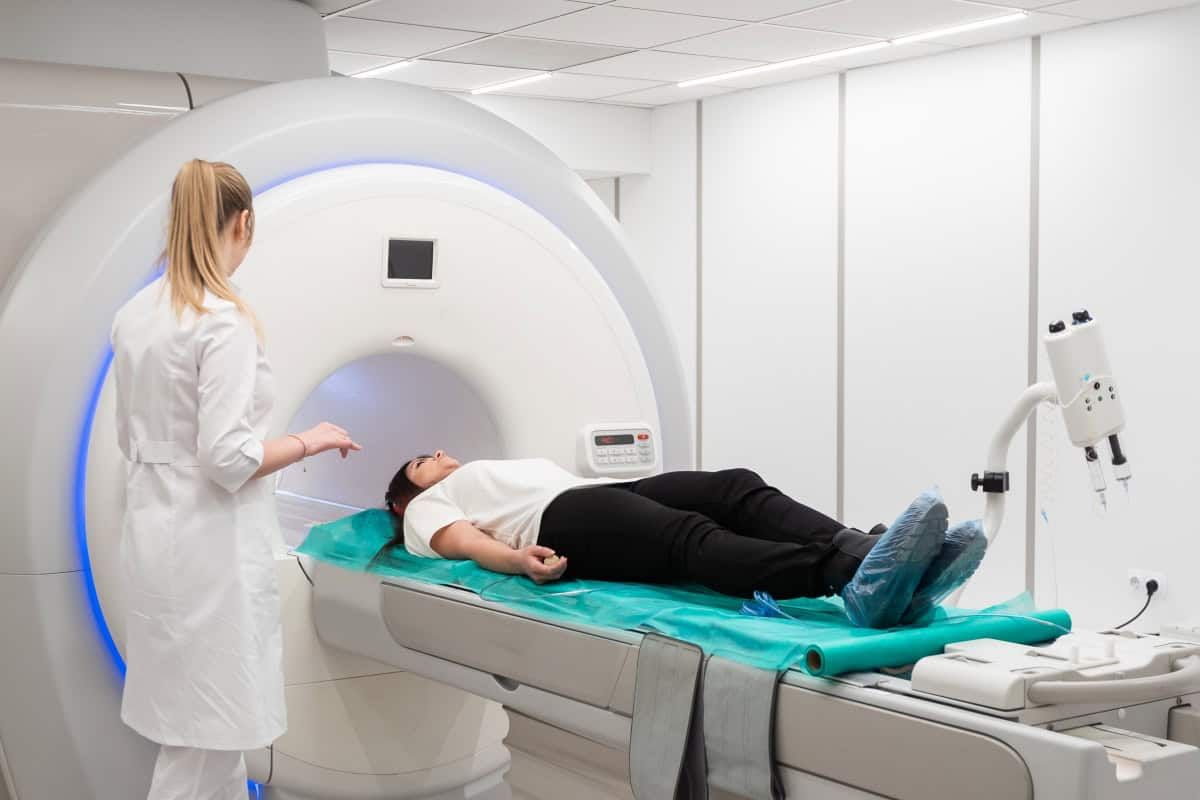 Een patiënt ligt op een bed van een MRI-machine, bedekt met een groen laken, terwijl een zorgprofessional in een witte jas in de buurt staat om de scan voor te bereiden in een moderne medische faciliteit.